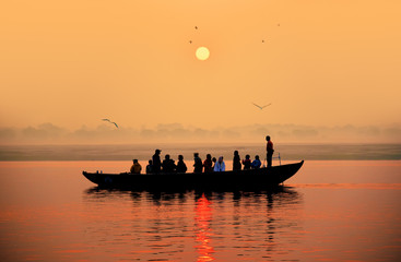 Naklejka premium Beautiful orange colored sunset on a Ganges river with a silhouette of a boat and people.