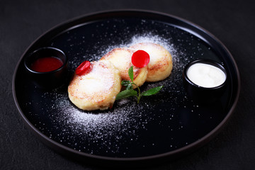 Cottage cheese pancakes with jam and sour cream, syrniki on black plate. Ukrainian or russian traditional cuisine, sweet and nutritional breakfast