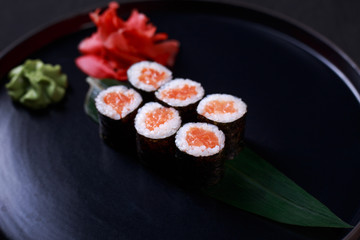 restaurant menu, delicious traditional seafood. maki roll with salmon, served on black plate, close up