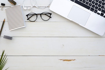 Home office workspace with laptop, glasses, palm leaf, earpligs, notebook and office accessories....