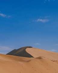 Fototapeta na wymiar Sand dunes and desert under blue sky at Mingsha Mountain, in Dunhuang, Gansu, China