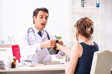 Young doctor checking woman's blood pressure