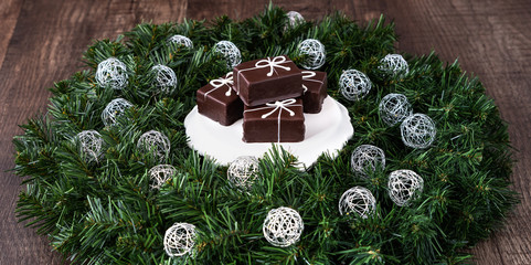 Individual Christmas present chocolate cakes on a white plate, in a wreath with LED Christmas lights on a wood background