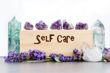 Self Care - word burnt in wood with purple lavender flowers, amethyst, fluorite and quartz crystals on slate with white background