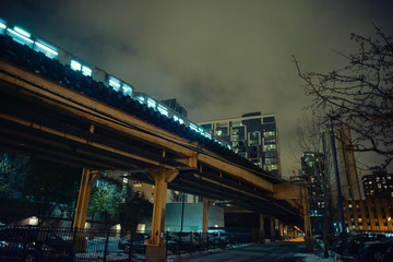 Elevated subway train on a vintage urban city railway bridge with an alley during the winter at night