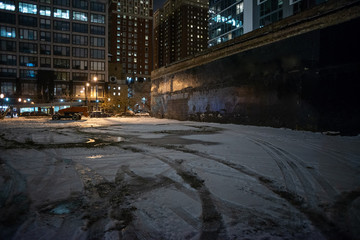 Scary industrial urban street city night winter scene with a vintage factory warehouse and a decaying billboard over an empty parking lot © Bruno Passigatti