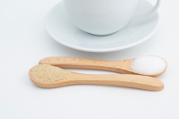 Part of white ceramic drink cup with white and brown sugar in wooden spoon, close up