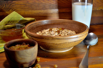Porridge in a ceramic plate, milk, honey, raisins on a wooden background.