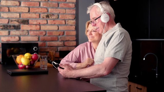 senior, happy couple listening to music on cellphone by table in the kitchen
