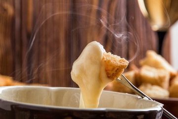 Close up, macro. Traditional french cheese fondue. Crouton dipped into stemy-hot cheese fondue on a...