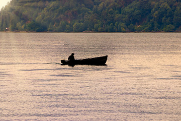 guy in a boat silloughetted against calm water
