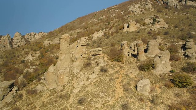 Beautiful autumn landscape with unusual rocks and hills in a sunny day. Shot. Mountains with bizarre form peaks on withered, yellow hills background.