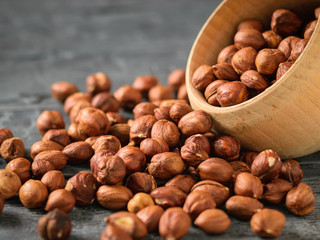 Hazelnut kernels are poured from a wooden bowl on a dark table.