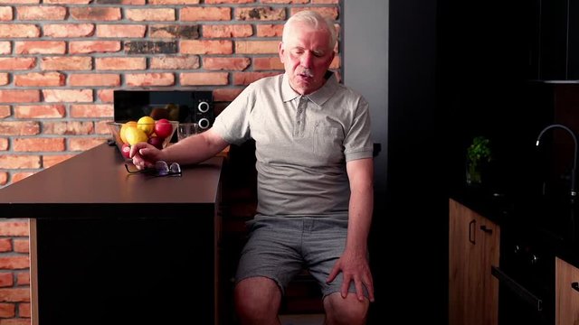 Senior, tired man having backbone pain sitting by table at home
