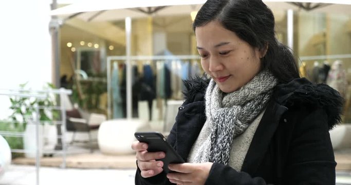 Chinese woman playing with a cellphone outside a couture and smilling