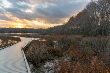 A wooden boardwalk winds through a barren marshland while a wonderful display of colors dance across the twilight sky.