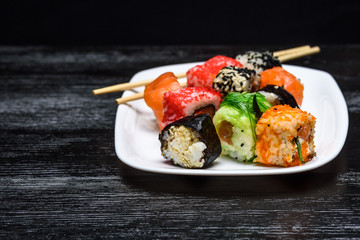 Sushi on a plate on a black wooden background.