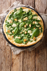 Italian cuisine thin pizza with fresh spinach, garlic and cheese close-up on a board. Vertical top view