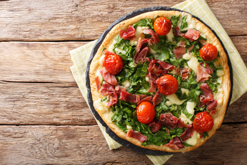 Freshly cooked hot pizza with spinach, tomatoes, prosciutto and cheese close-up on the table. horizontal top view