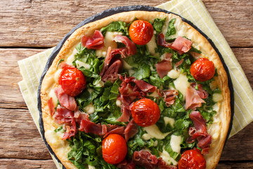 Italian white pizza with spinach, tomatoes, prosciutto and cheese close-up on the table. Horizontal top view