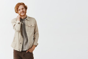 Waist-up shot of shy good-looking and frienly redhead guy with beard and wavy hair touching neck...
