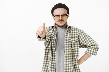 You guilty. Serious-looking strict, irritated young male music teacher in black beanie and glasses with moustache standing in furious pose pointing at camera dissatisfied blaming student