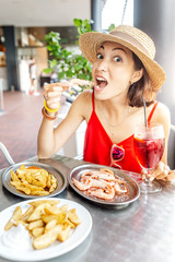 Happy Asian woman in hat eating local Spanish cuisine grilled seafood and prawns