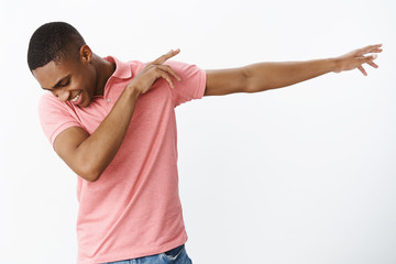 Satisfied happy and charismatic joyful african american young guy making dab pulling hands right tilting, looking down with broad happy smile dancing, having fun over gray background