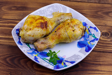 Baked chicken drumsticks with potatoes in a plate on wooden table