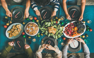Company of friends of different ages gathering for Christmas or New Year party dinner at festive table. Flat-lay of people sitting with plates and ready to start celebrating holiday together, top view