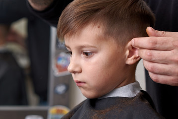 Boy getting haircut by hairdresser in barbershop.