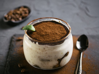 High angle view of tiramisu in glass cup on stone plate over black concrete background, Copy space.