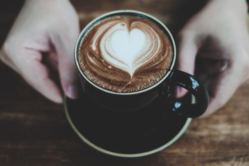 Hands holding cup of hot coffee with heart shaped foam, warm color tone , good service coffee shop