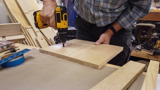 4k clip of a man drilling holes in a piece of oak wood in his wood shop; DIY carpentry theme