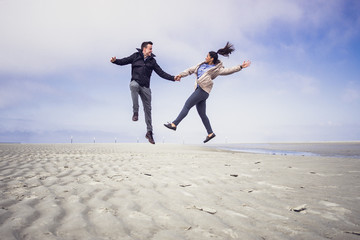 Happy young couple jumping in the air at a northern sea beach in Germany.