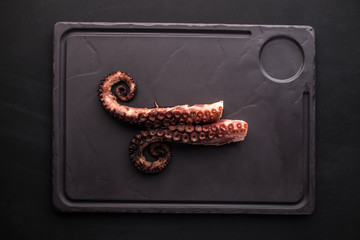 grilled octopus legs on stone board on black background © Eduard Zhukov