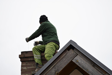 Chimney sweep man cleaning brown brick chimney on building roof on clear sky background with copy...