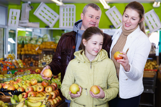 Loving parents with happy daughter choosing sweet ripe apple