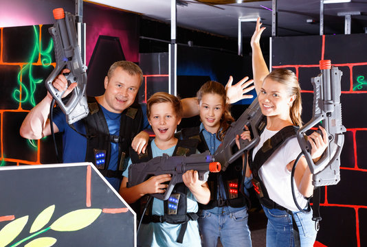 Group of happy teenagers and adults with laser guns posing together while having fun on lasertag arena