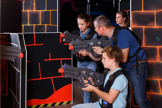 positive young parents and children with laser pistols playing laser tag