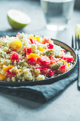 Couscous salad with fresh red and yellow bell peppers, avocado, tomatoes and lime. The concept of vegetarian and healthy food.