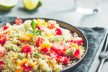 Couscous salad with fresh red and yellow bell peppers, avocado, tomatoes and lime. The concept of vegetarian and healthy food.