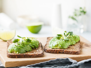 Two toasts with avocado on a wooden board on a breakfast table. The concept of vegetarian and healthy diet food.