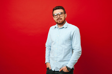 Photo of a young hipster man with hands in pockets over red background