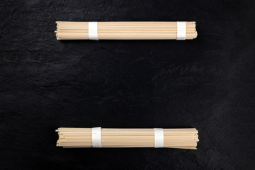 Two individually wrapped portions of udon noodles, shot from above on a black background with a place for text