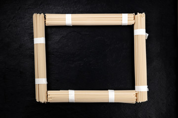 Obraz premium A photo of individually wrapped portions of udon noodles, shot from above, forming a frame on a black background with a place for text