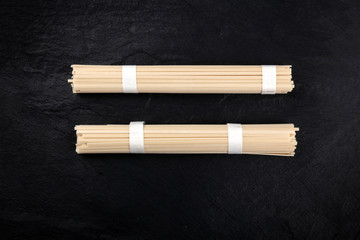 Two individually wrapped portions of udon noodles, shot from above on a black background with a place for text