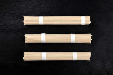 Three individually wrapped portions of udon noodles, shot from the top on a black background with a place for text