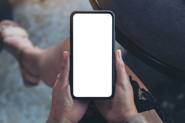 Top view mockup image of woman's hands holding black mobile phone with blank white screen while sitting in cafe