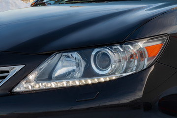 Black car with an engine close-up of front headlamp view with turn on daylight lamp